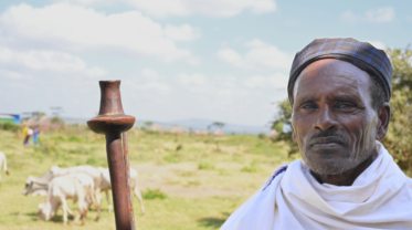 A pastoralist with a crook stands in front of his animals.