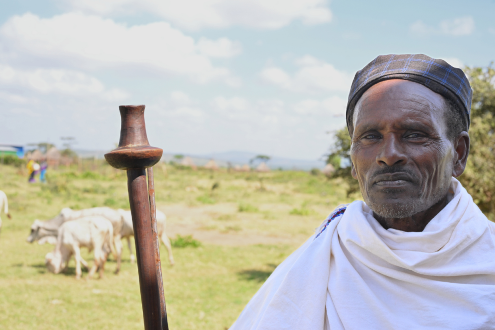 A pastoralist with a crook stands in front of his animals.